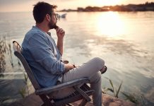 beardy guy sitting alone on a river coast, enjoying the sunset,
