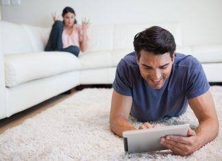 Man using a tablet computer while his girlfriend is getting mad at him