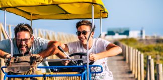 Mature man with teenage son riding cart on road during vacation. Father son enjoying leisure time on holidays. Father with son having fun driving trolley cart on holiday